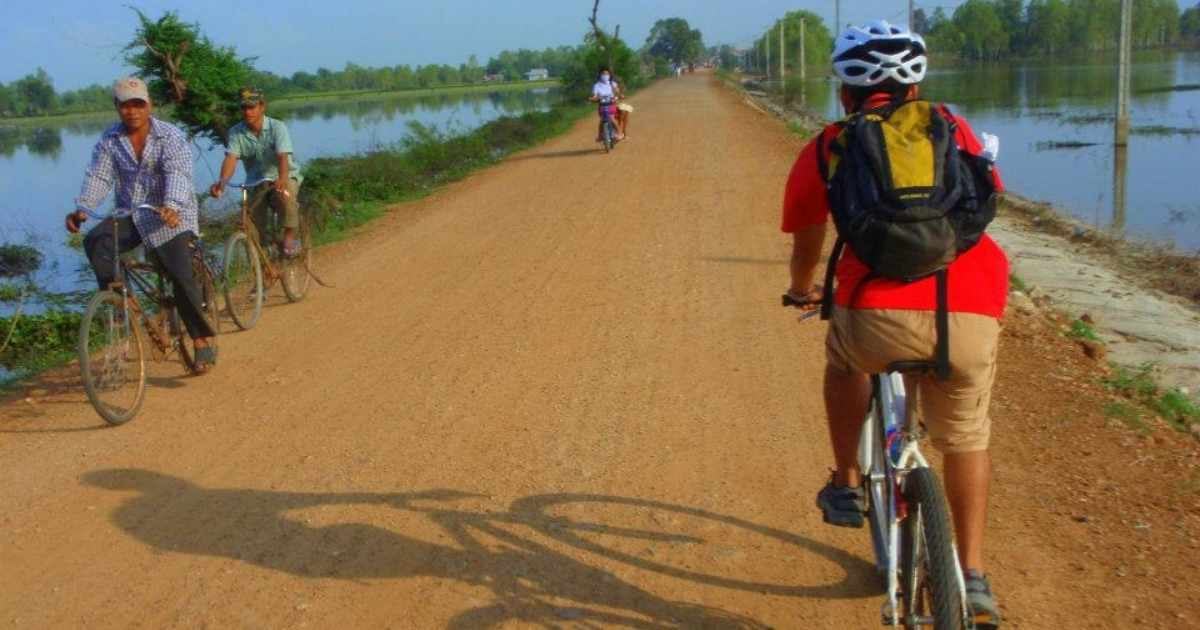 Top Alternative Christmas Getaways 4 Person cycling past local people in Cambodia